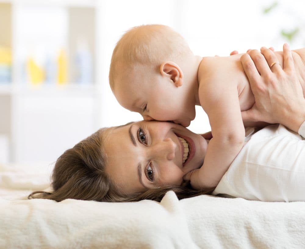 Mama lacht mit Baby auf dem Bett